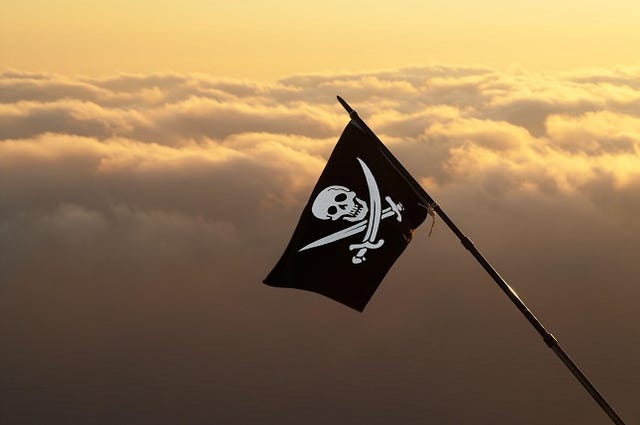 Jolly Roger (pirate flag) on wind and sea in sunset cloudy sky at background