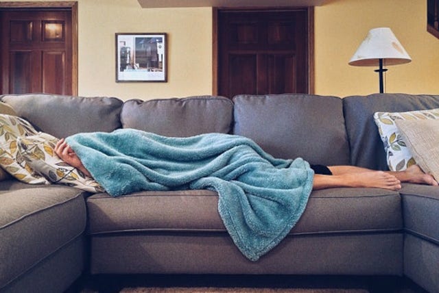 young adult crashed on a couch with blanket over