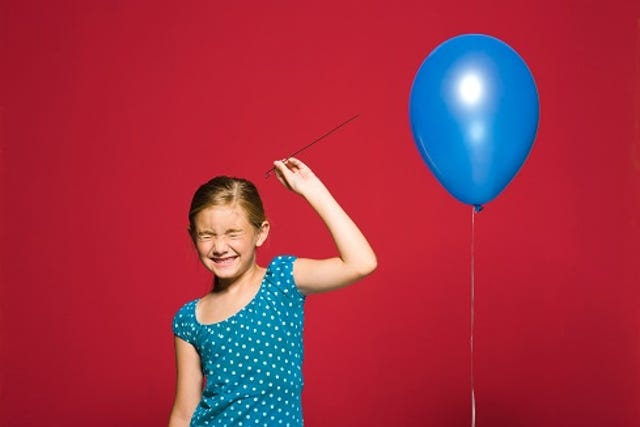 young girl with eyes closed ready to pop a blue balloon