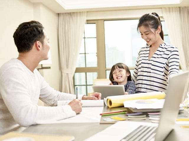 young asian family gathered at table working on laptops and tablets