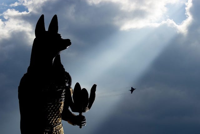 Statue of mythology jackal anubis inpu anup. In the background is a supersonic plane.