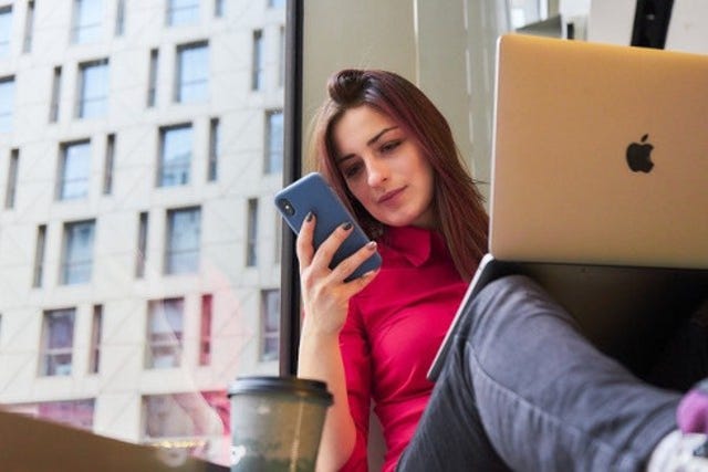 young, white female looking at her mobile phone while also working on her laptop