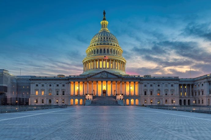 golden lights warm the inside of the Capitol building, which sits in front of a dusky sky