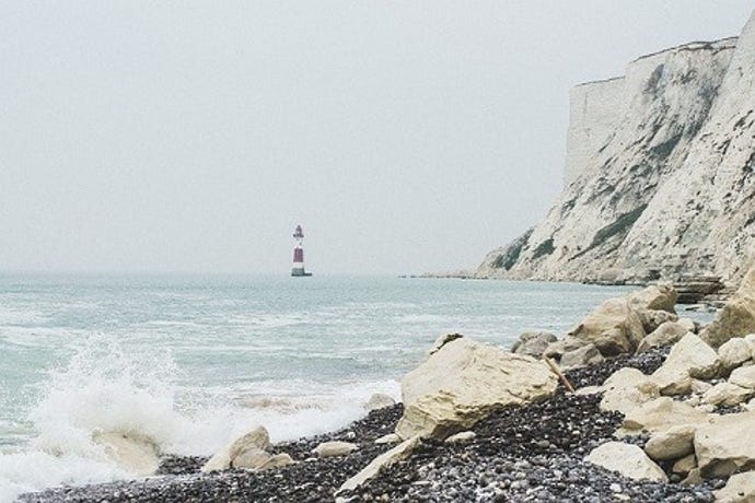 edge of a cliff on the ocean with a lighthouse in background