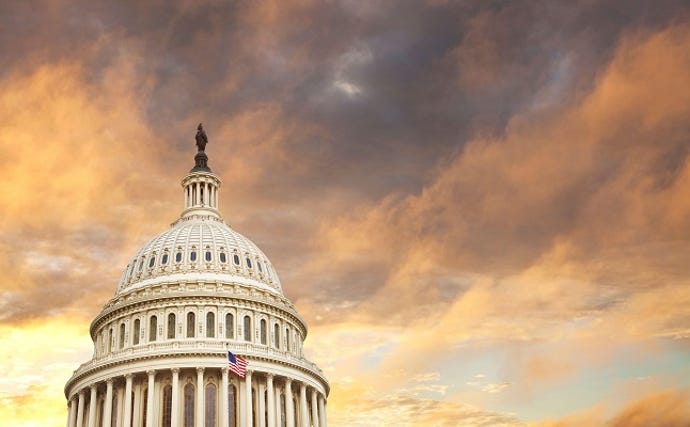 The dome of the United States capitol with an American flag and dramatic clouds behind